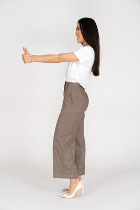 Side view of a smiling young lady in breeches and t-shirt showing thumb up