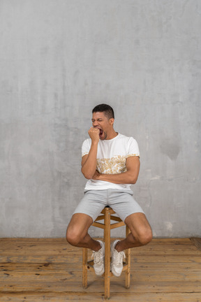 Young man sitting on stool and yawning