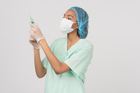 Enfermeira na máscara facial, verificando a seringa