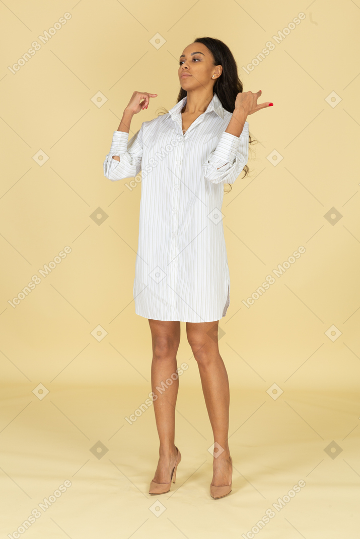 Вид в три четверти темнокожей молодой девушки в белом платье, поправляющей прическу