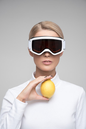 Young blonde woman in ski goggles holding lemon