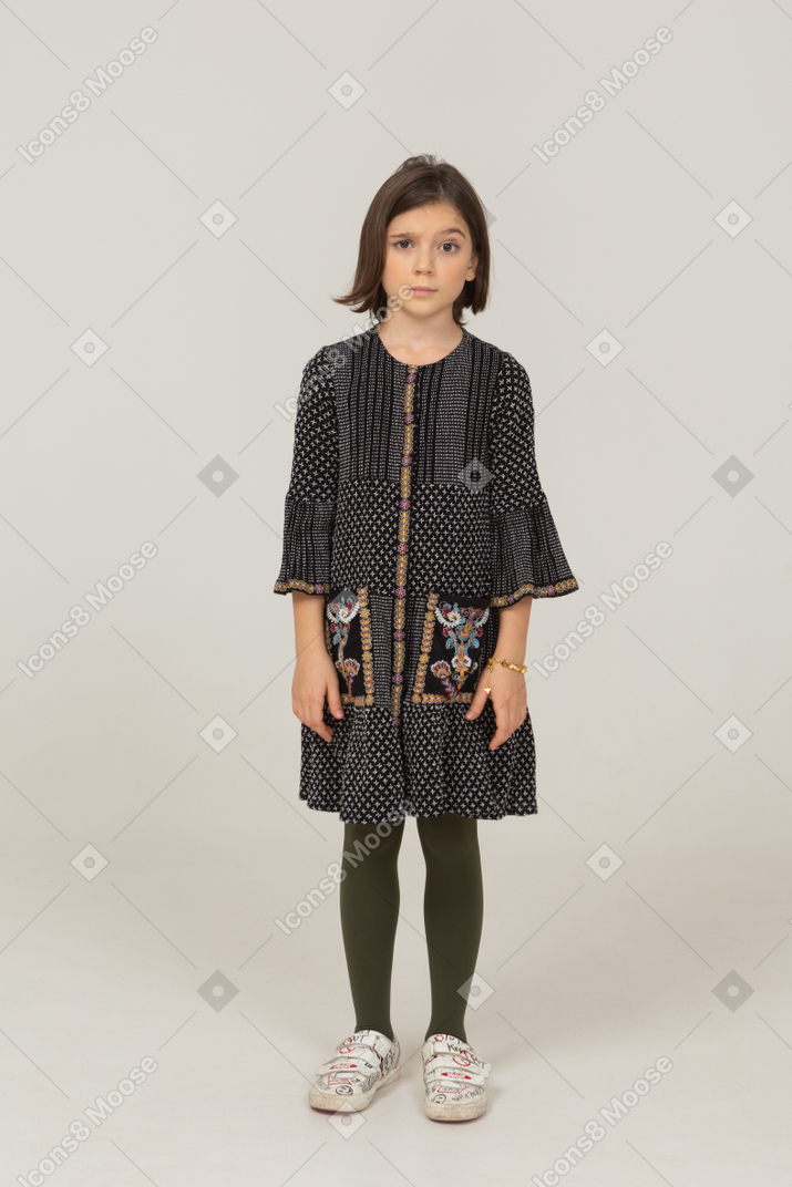 Озадаченная маленькая девочка в платье, подняв бровь, вид спереди