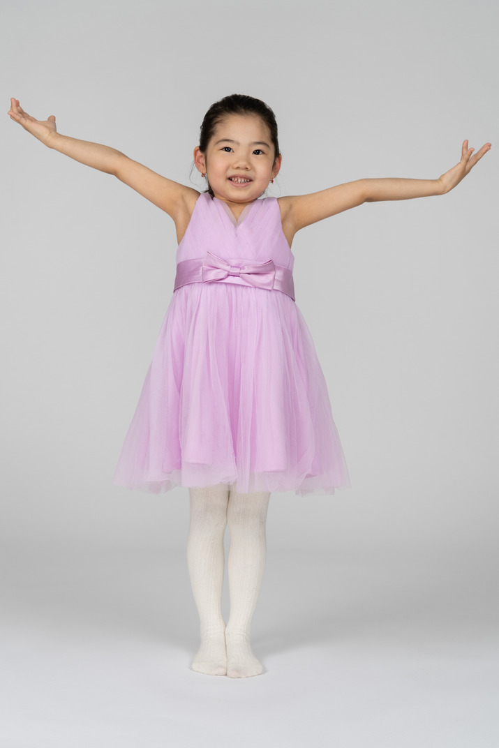 Little girl in pink dress standing with standing arms