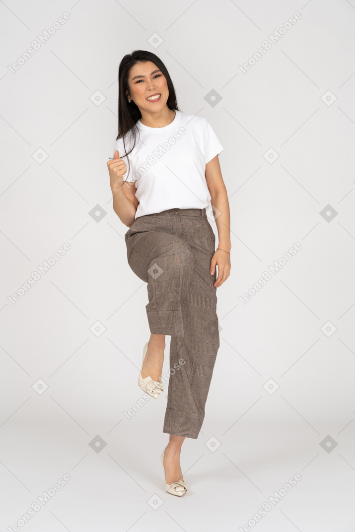 Vista frontale di una giovane donna sorridente in calzoni e t-shirt alzando la gamba