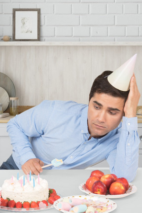 Hombre en la mesa con una cuchara mirando el pastel de cumpleaños