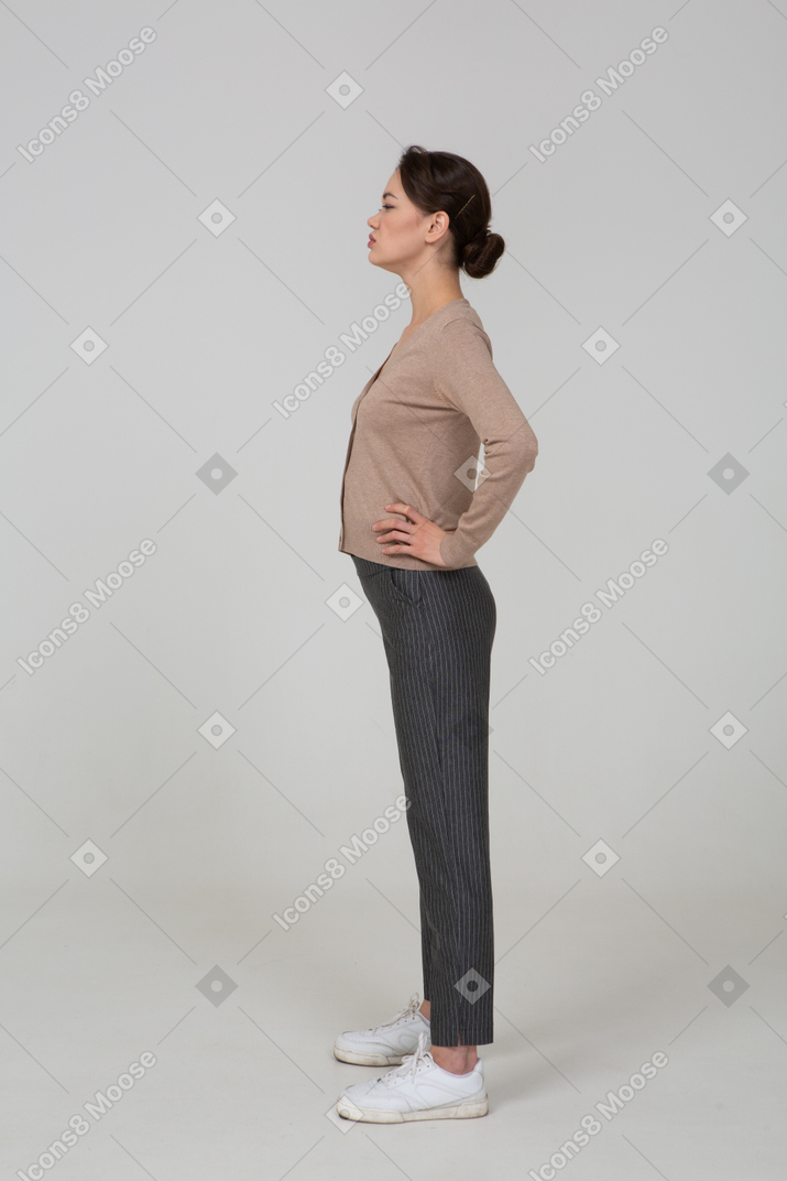 Side view of a displeased young lady in pullover and pants putting hands on hips