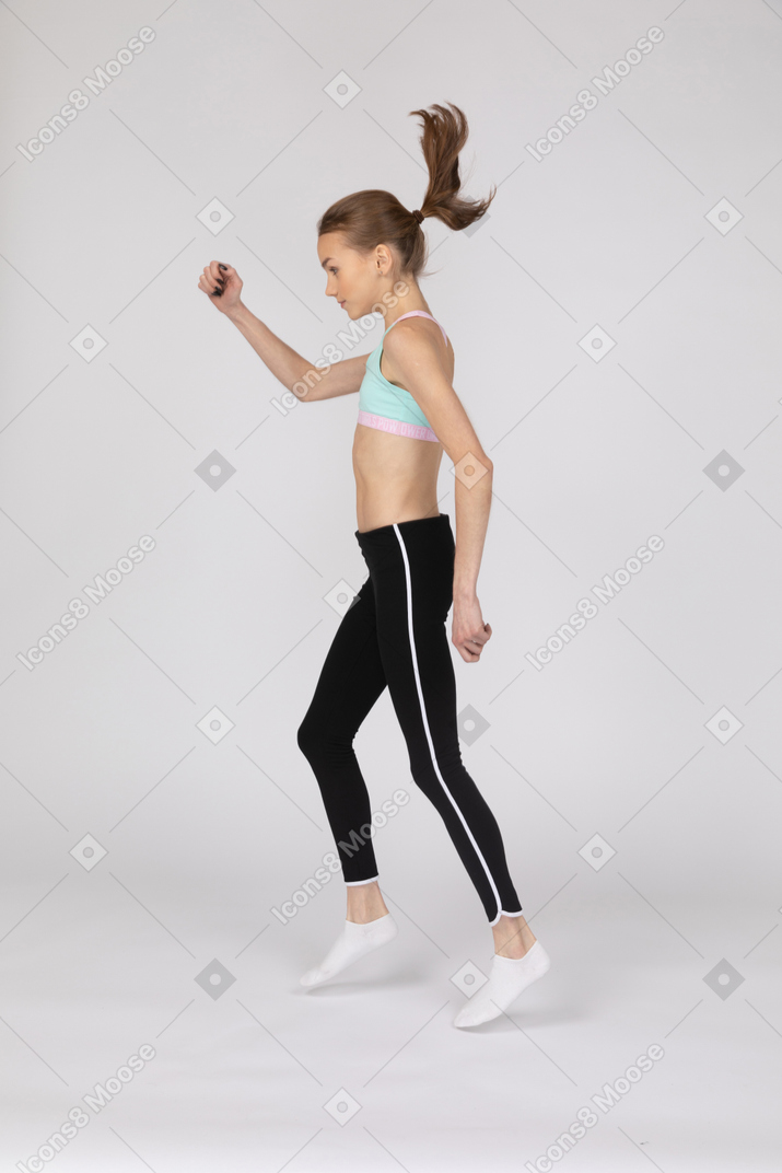 Side view of a teen girl in sportswear raising hand and dancing