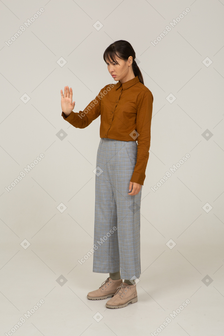 Vista di tre quarti di una giovane donna asiatica in calzoni e camicetta che allunga il braccio