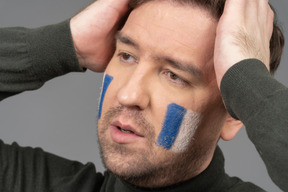 A portrait of a football fan with blue & white face art raising hands