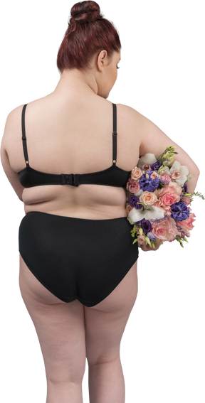 Corpo positivo feminino em lingerie preta posando de volta para a câmera com um buquê de flores