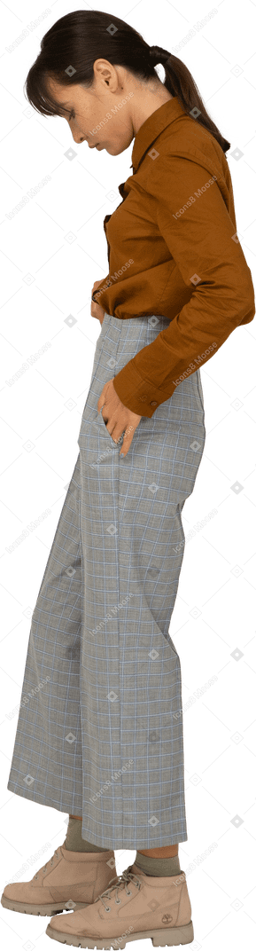 Vista lateral de una joven mujer asiática en calzones y blusa poniendo las manos en los bolsillos