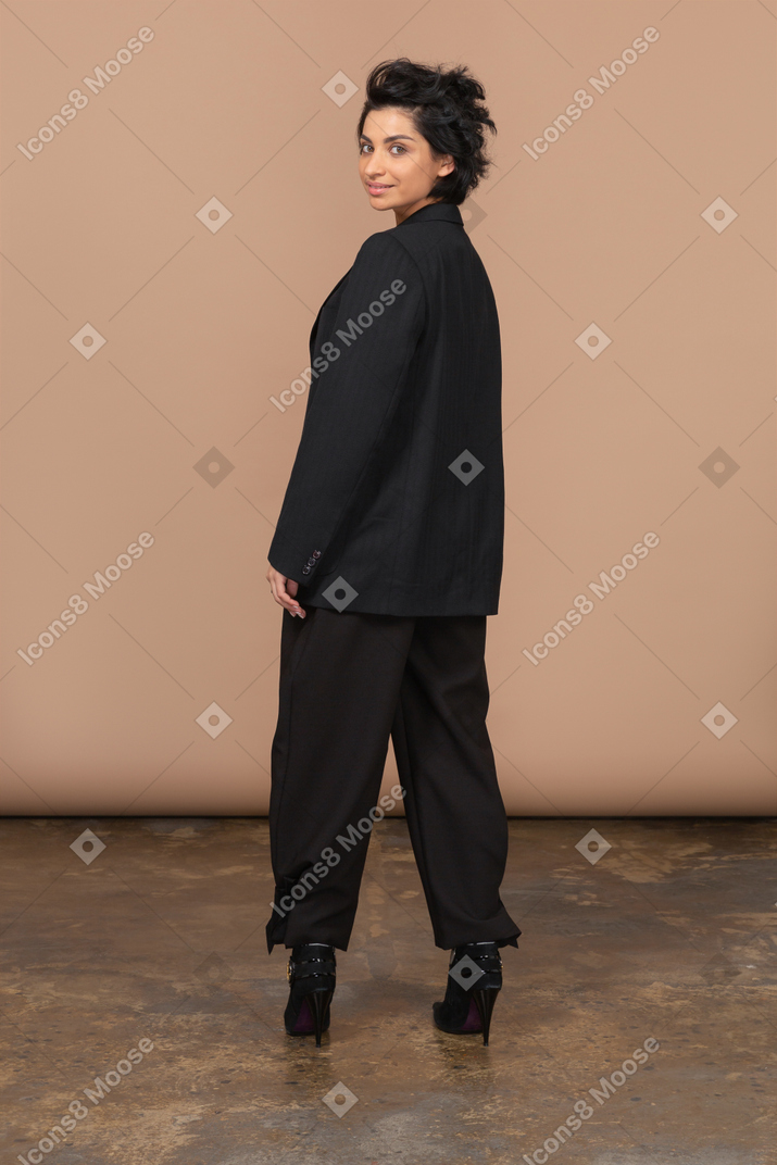 Rückansicht einer geschäftsfrau, die schwarzen anzug trägt und kamera betrachtet