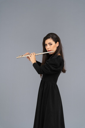 Side view of a serious young lady in black dress playing the flute