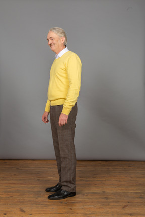 Vista di tre quarti di un vecchio sorridente in pullover giallo e guardando da parte