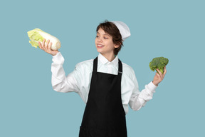 Kid boy chef holding chinese cabbage and broccoli