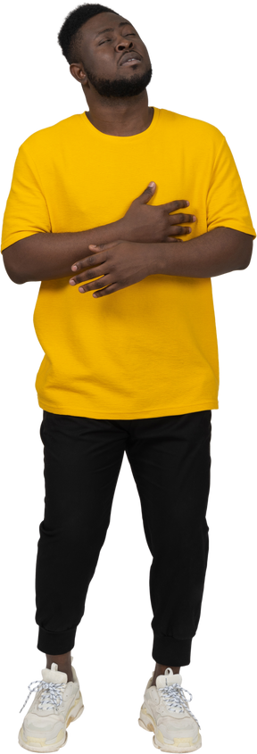 一个身穿黄色 t 恤、手放在肚子上的黑皮肤年轻男子的前视图