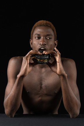 Front view of a young afro man biting a burger