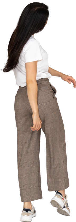 Vista posteriore di tre quarti di una giovane donna in calzoni e maglietta che si allontana
