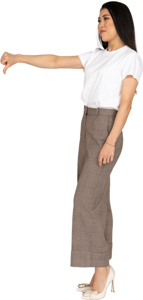 Vista di tre quarti di una giovane donna in calzoni e maglietta che mostra il pollice verso il basso