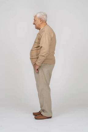 Side view of an old man in casual clothes standing with hands in pockets
