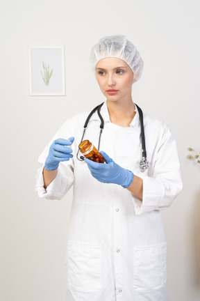 Vista frontal de uma jovem médica abrindo um frasco de comprimidos