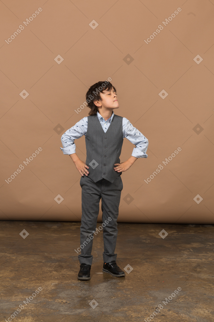Vista frontal de un niño con traje gris posando con las manos en las caderas