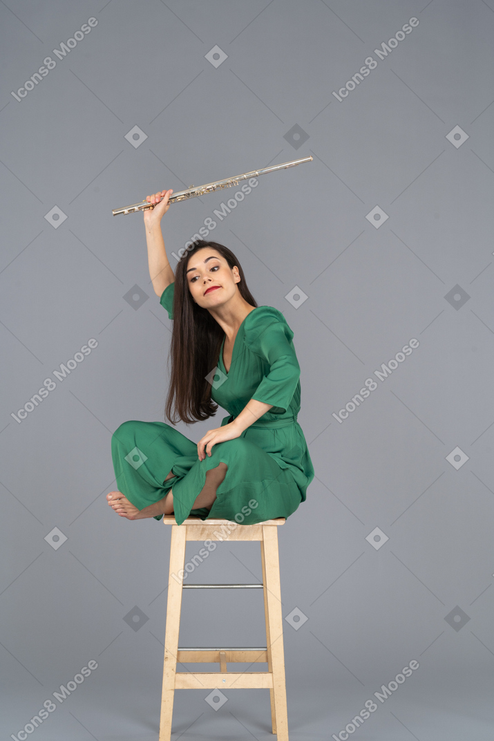 Dreiviertelansicht einer verrückten klarinettenspielerin, die mit gekreuzten beinen auf einem stuhl sitzt