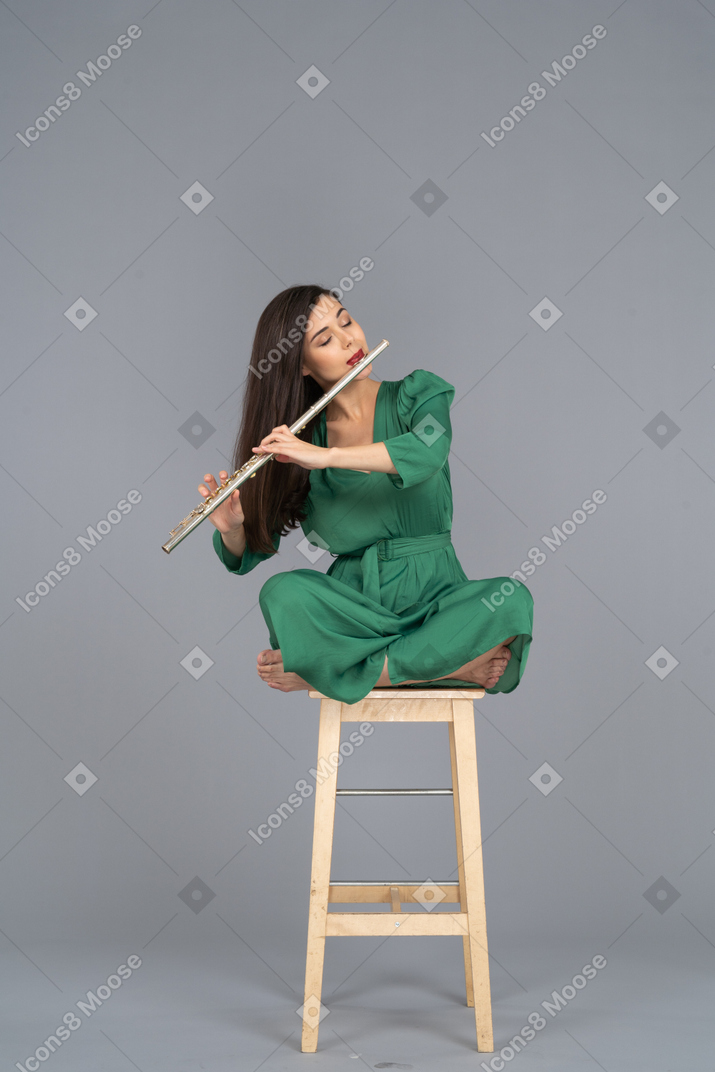 Девушка в полный рост, играющая на кларнете, сидящая со скрещенными ногами на деревянном стуле