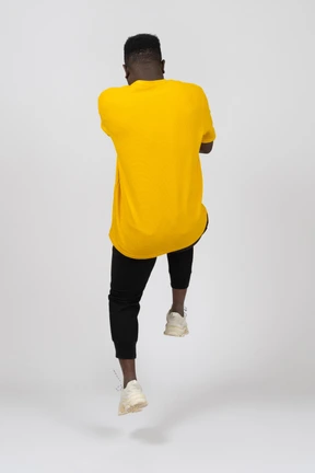 Vista posterior de un joven de piel oscura con camiseta amarilla saltando hacia atrás