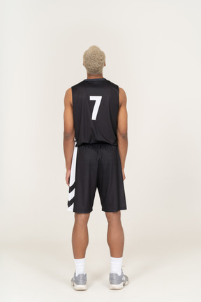 Vista posteriore di un giovane giocatore di basket maschile in piedi immobile e guardando in alto