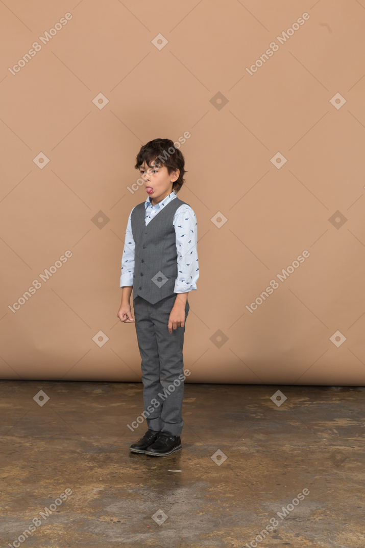 Vista frontal de um menino de terno cinza fazendo caretas