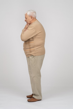 Vista laterale di un vecchio premuroso in abiti casual in piedi con la mano sul mento