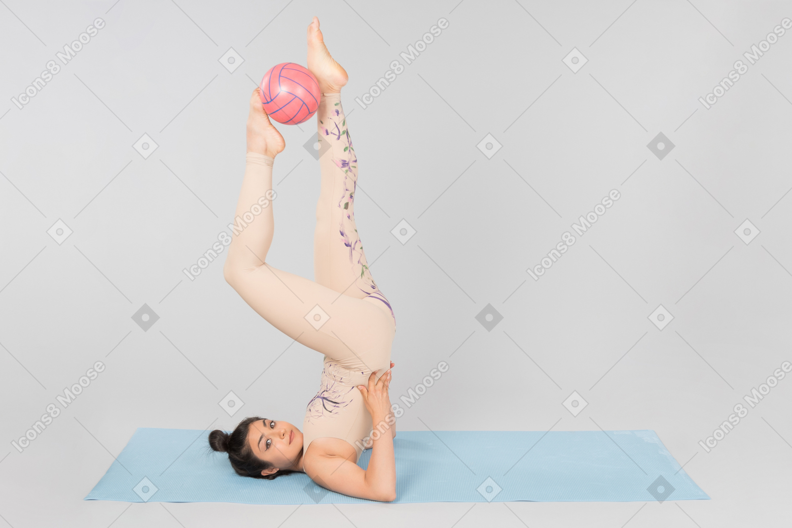 Young indian gymnast lying on yoga mat on the back and holding ball up with legs