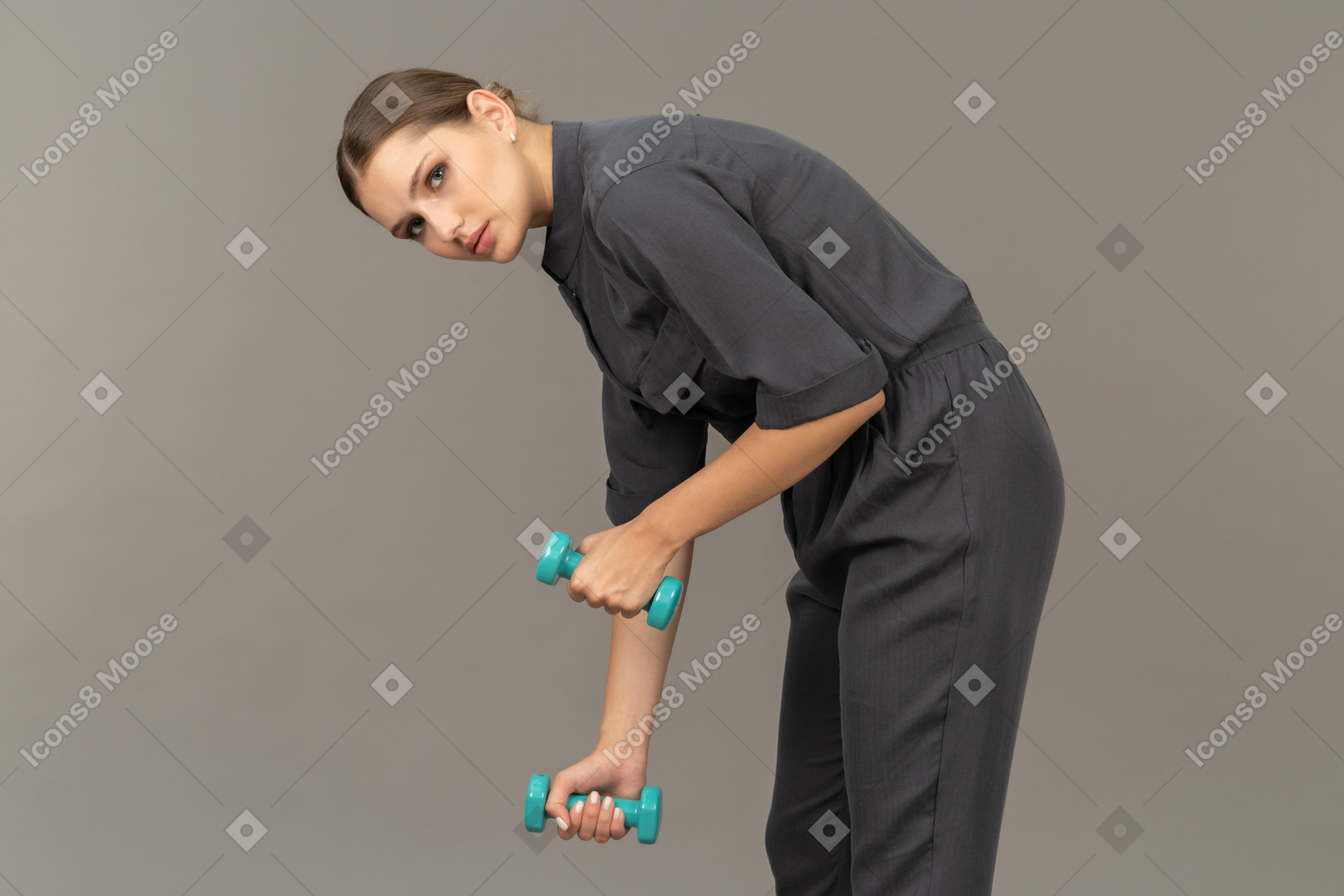 Вид сбоку молодой женщины в комбинезоне, делающей упражнения с гантелями