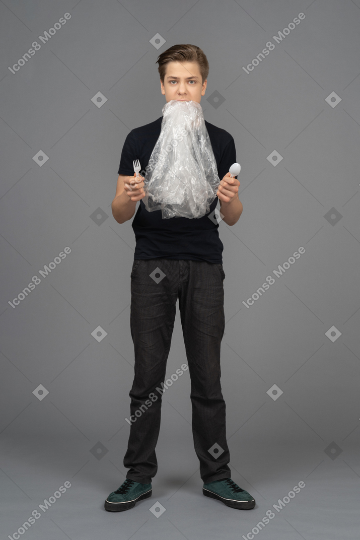 Modello maschile in possesso di forchetta e cucchiaio di plastica con pellicola trasparente in bocca