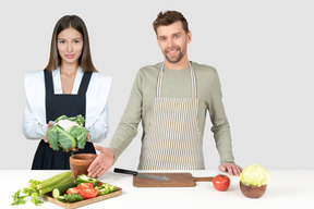 A man and woman standing next to a cutting board with vegetables