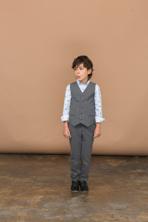 Vista frontal de un chico lindo en traje gris mirando a un lado