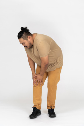 Hombre asiático de talla grande agachándose para tocar la rodilla lastimada