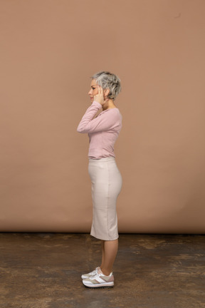 Vista lateral de una mujer en ropa casual cubriendo las orejas con las manos