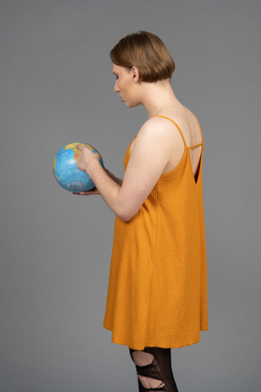 Back view of a young transgender person pointing somewhere on globe