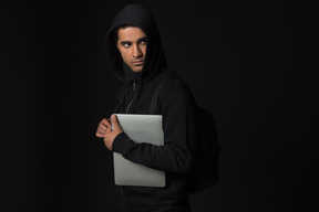 Hackerkerl, der in der dunkelheit steht und laptop hält
