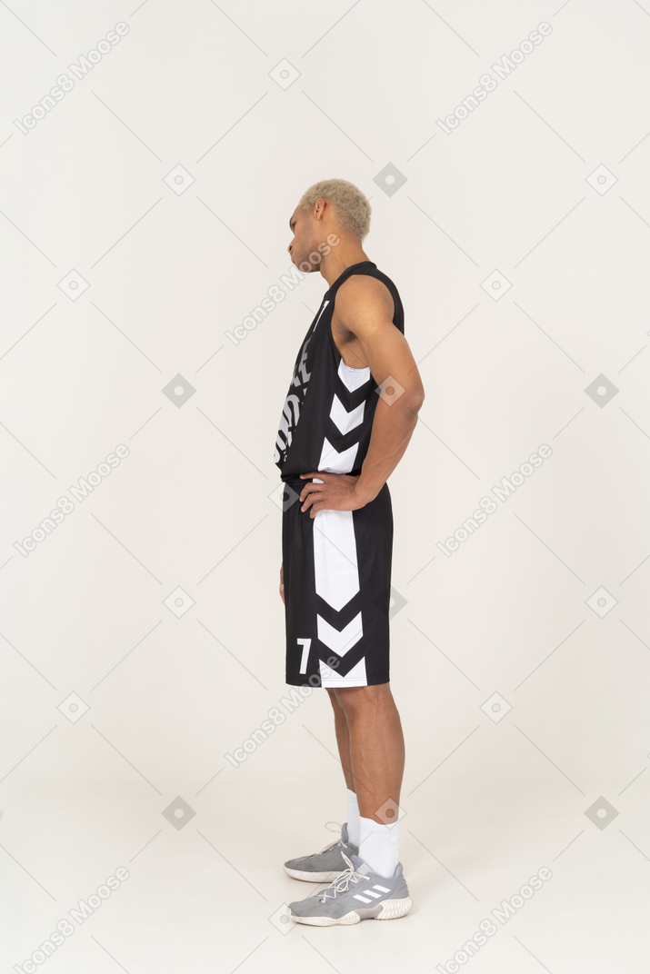 Side view of a young male basketball player putting hands on hips & tilting head