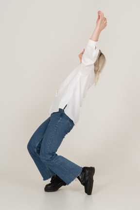 Side view of a blonde female in casual clothes on her tiptoes falling and raising hands