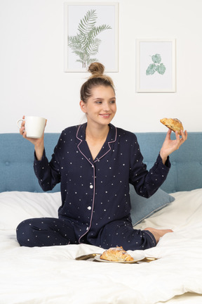 一位穿着睡衣的年轻女士在床上吃早餐的前视图