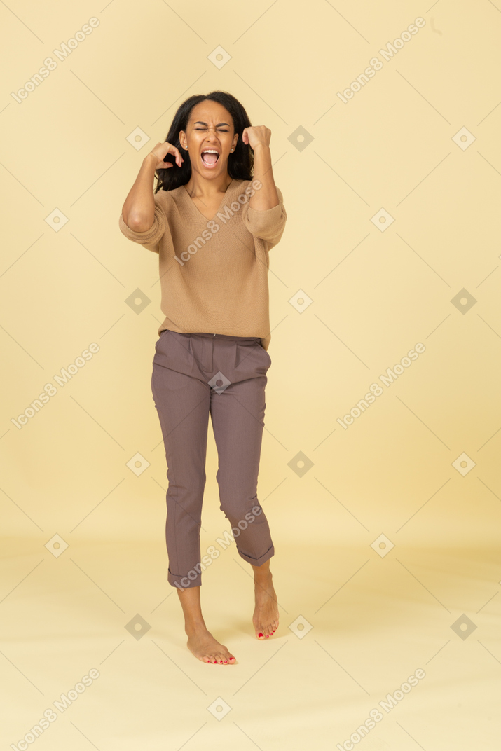 Vista frontal de uma jovem mulher de pele escura gritando e levantando as mãos
