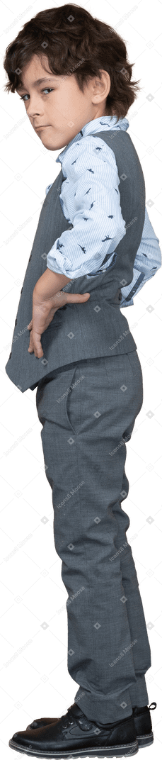 Vista lateral de un chico lindo con traje gris posando con las manos en las caderas