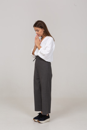 Vista di tre quarti di una giovane donna in preghiera in abiti da ufficio che si tiene per mano insieme