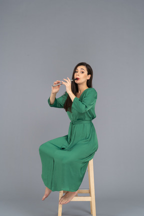 Full-length of a young lady in green dress sitting on a chair while playing the clarinet