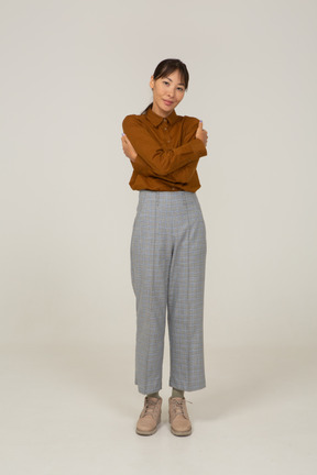 Front view of a young asian female in breeches and blouse embracing herself