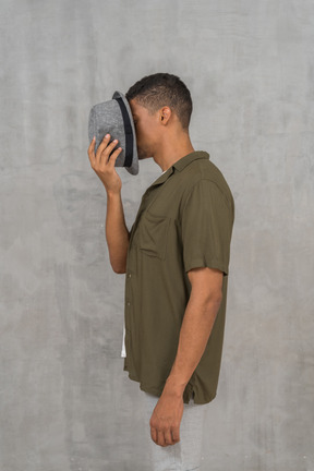 Side view of man in casual clothes covering his face with hat